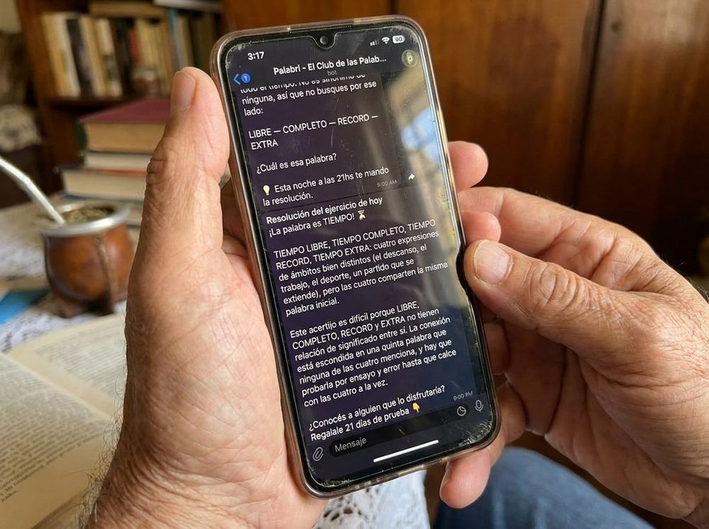 Una persona mayor lee en su celular la resolución del ejercicio de Palabri, con el mate al lado